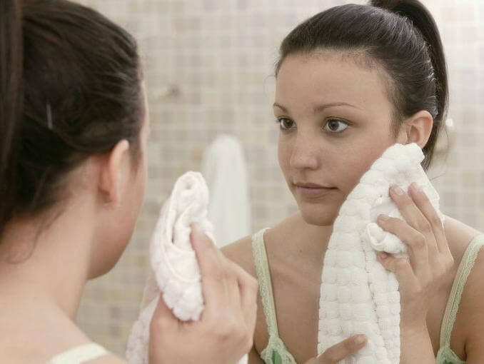 дівчина витирає лице рушником перед дзеркалом
