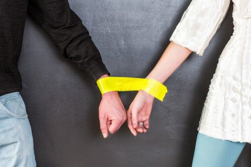 руки чоловіка та жінки зв'язані жовтою стрічкою